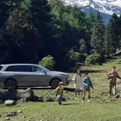 Familie vor einem silbernen Li L9 SUV in einer Waldlandschaft mit Bergen im Hintergrund.
