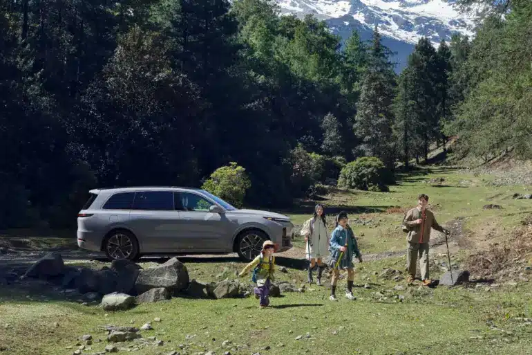 Familie vor einem silbernen Li L9 SUV in einer Waldlandschaft mit Bergen im Hintergrund.