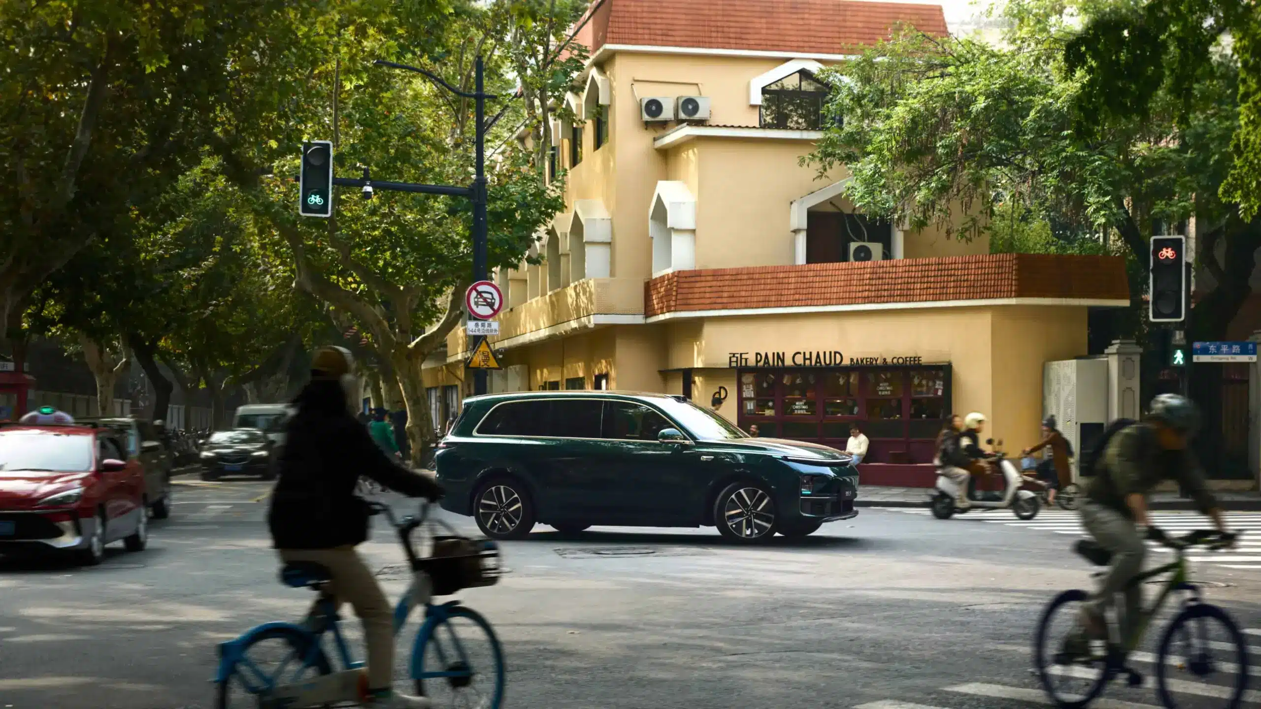 Dunkelgrüner Li L9 SUV fährt an einer Straßenkreuzung in einer Stadt vorbei.