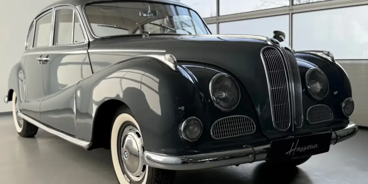 BMW 502 V8 Barockengel Baujahr 1959 in dunkelgrau, Seitenansicht mit Schiebedach und charakteristischer Kühlerfigur in einer hellen Ausstellungshalle