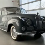 BMW 502 V8 Barockengel Baujahr 1959 in dunkelgrau, Seitenansicht mit Schiebedach und charakteristischer Kühlerfigur in einer hellen Ausstellungshalle