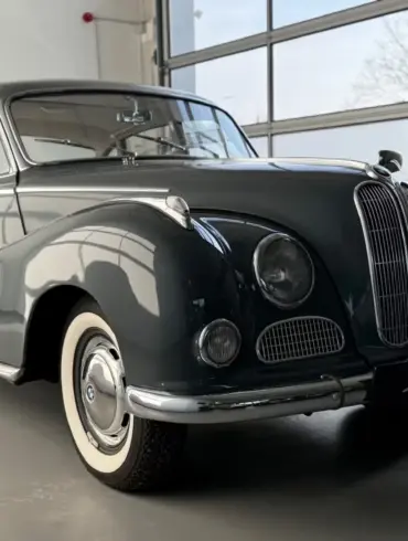 BMW 502 V8 Barockengel Baujahr 1959 in dunkelgrau, Seitenansicht mit Schiebedach und charakteristischer Kühlerfigur in einer hellen Ausstellungshalle
