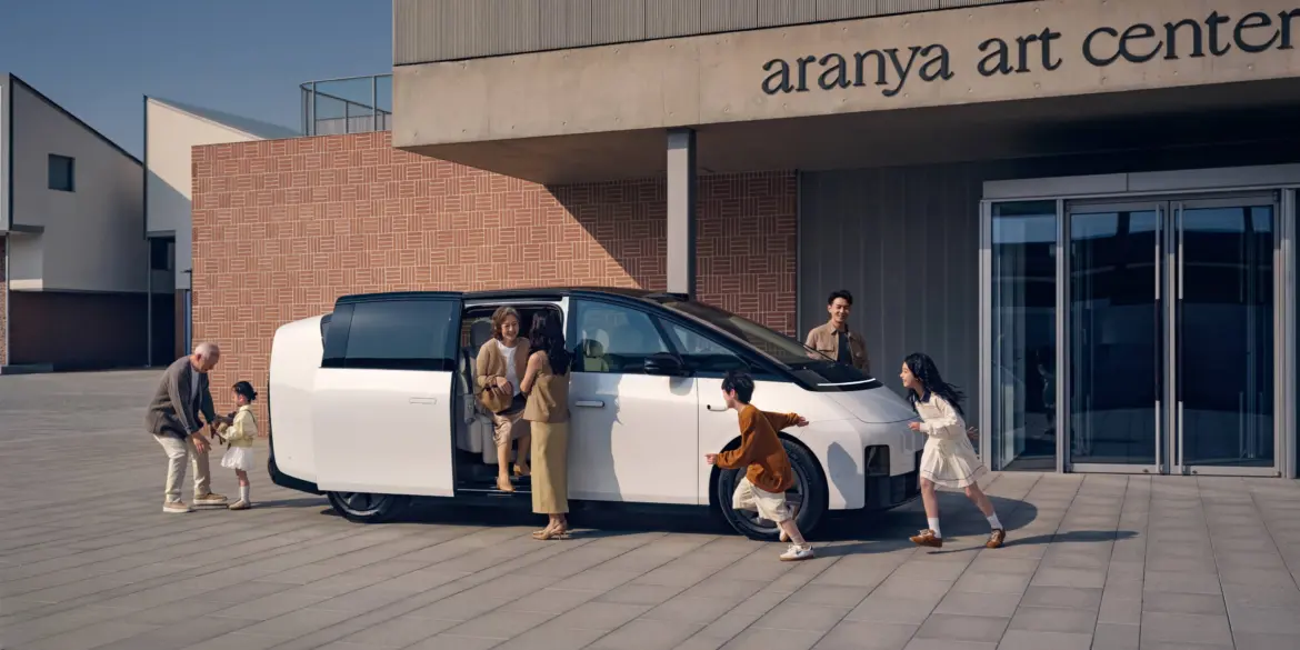 Weißer Li MEGA Elektro-Van mit geöffneter Schiebetür, mehrere Menschen verschiedener Generationen steigen ein und aus, modernes Gebäude im Hintergrund.