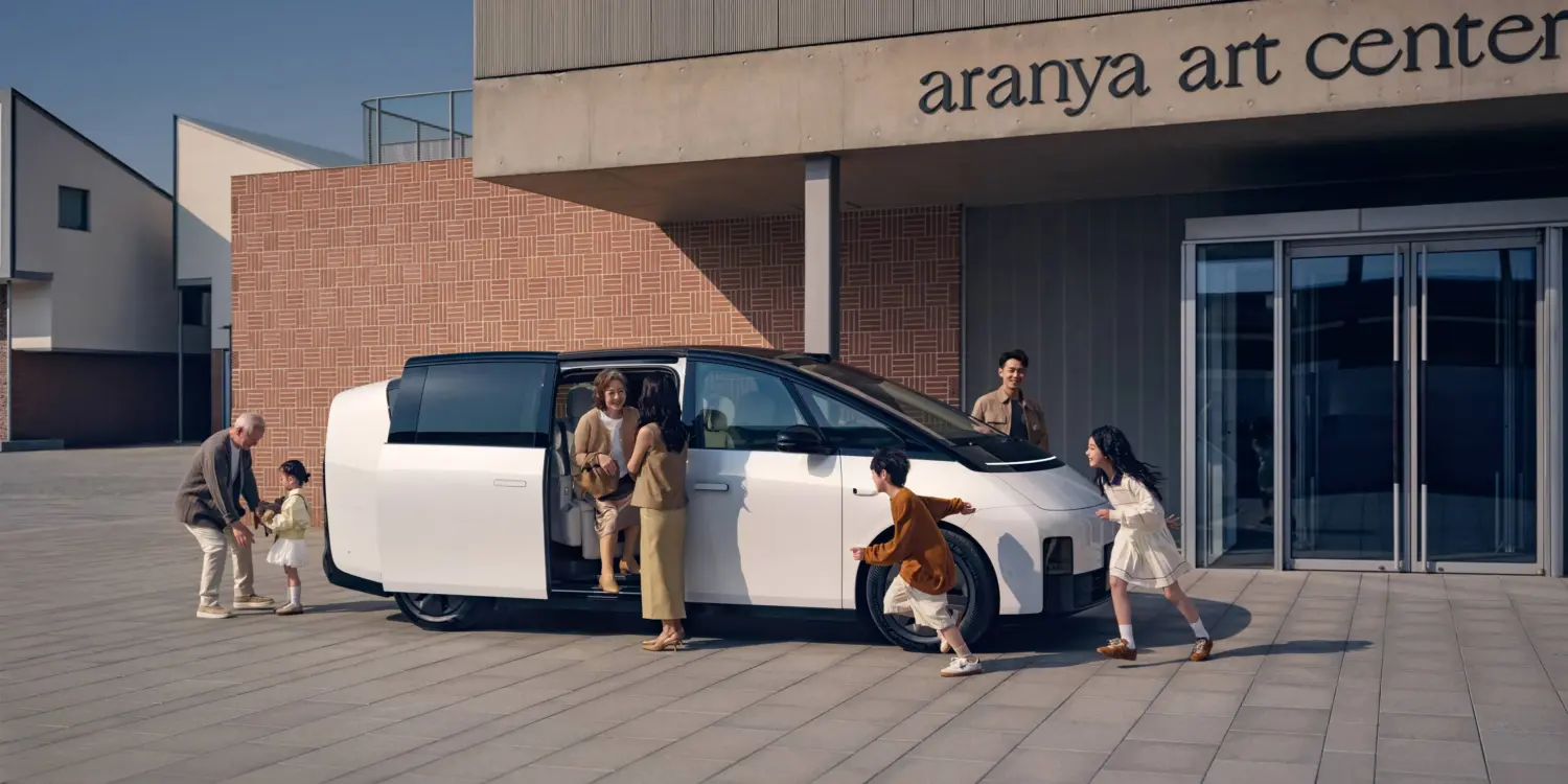 Weißer Li MEGA Elektro-Van mit geöffneter Schiebetür, mehrere Menschen verschiedener Generationen steigen ein und aus, modernes Gebäude im Hintergrund.