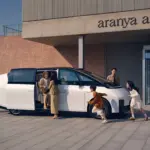 Weißer Li MEGA Elektro-Van mit geöffneter Schiebetür, mehrere Menschen verschiedener Generationen steigen ein und aus, modernes Gebäude im Hintergrund.