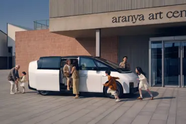 Weißer Li MEGA Elektro-Van mit geöffneter Schiebetür, mehrere Menschen verschiedener Generationen steigen ein und aus, modernes Gebäude im Hintergrund.