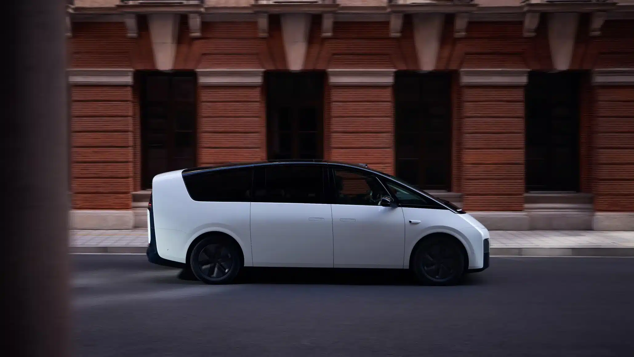 Seitenansicht des Li MEGA Elektro-Vans vor einem Backsteingebäude in der Stadt.