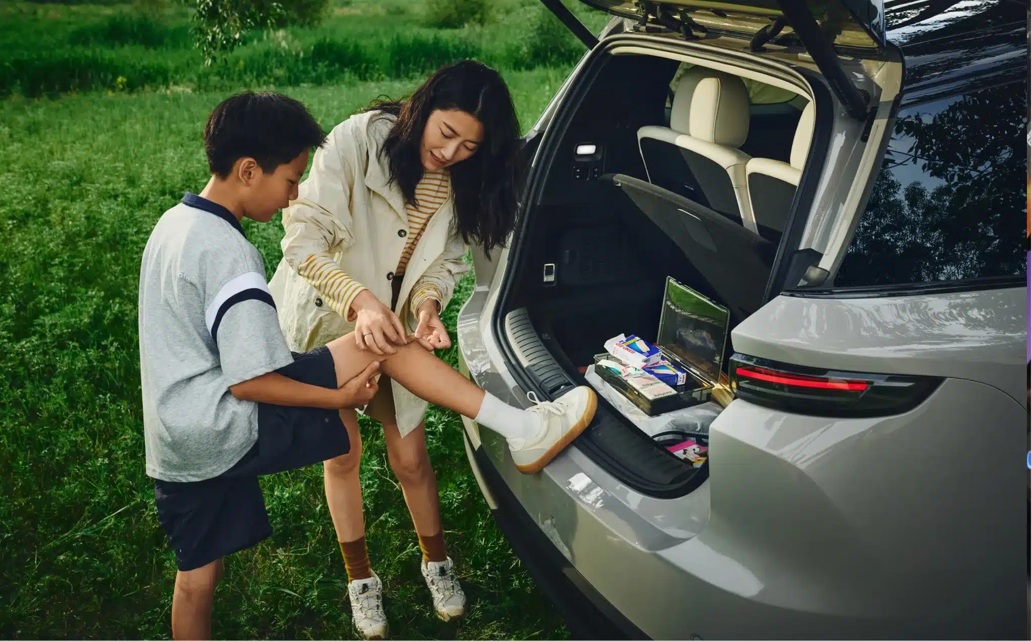 Familie am geöffneten Kofferraum des Li i8 SUV beim Versorgen einer kleinen Verletzung, Kofferraum mit Alltagsgegenständen.