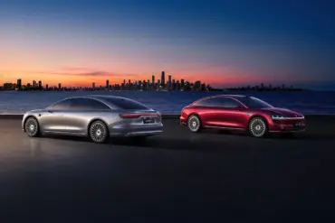 Zwei Xiangjie S9 Limousinen (silber und rot) stehen bei Sonnenuntergang vor einer Stadt am Wasser.