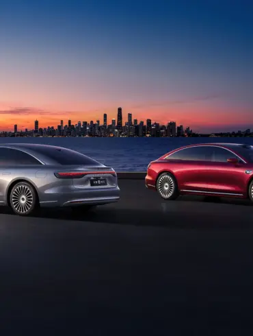 Zwei Xiangjie S9 Limousinen (silber und rot) stehen bei Sonnenuntergang vor einer Stadt am Wasser.