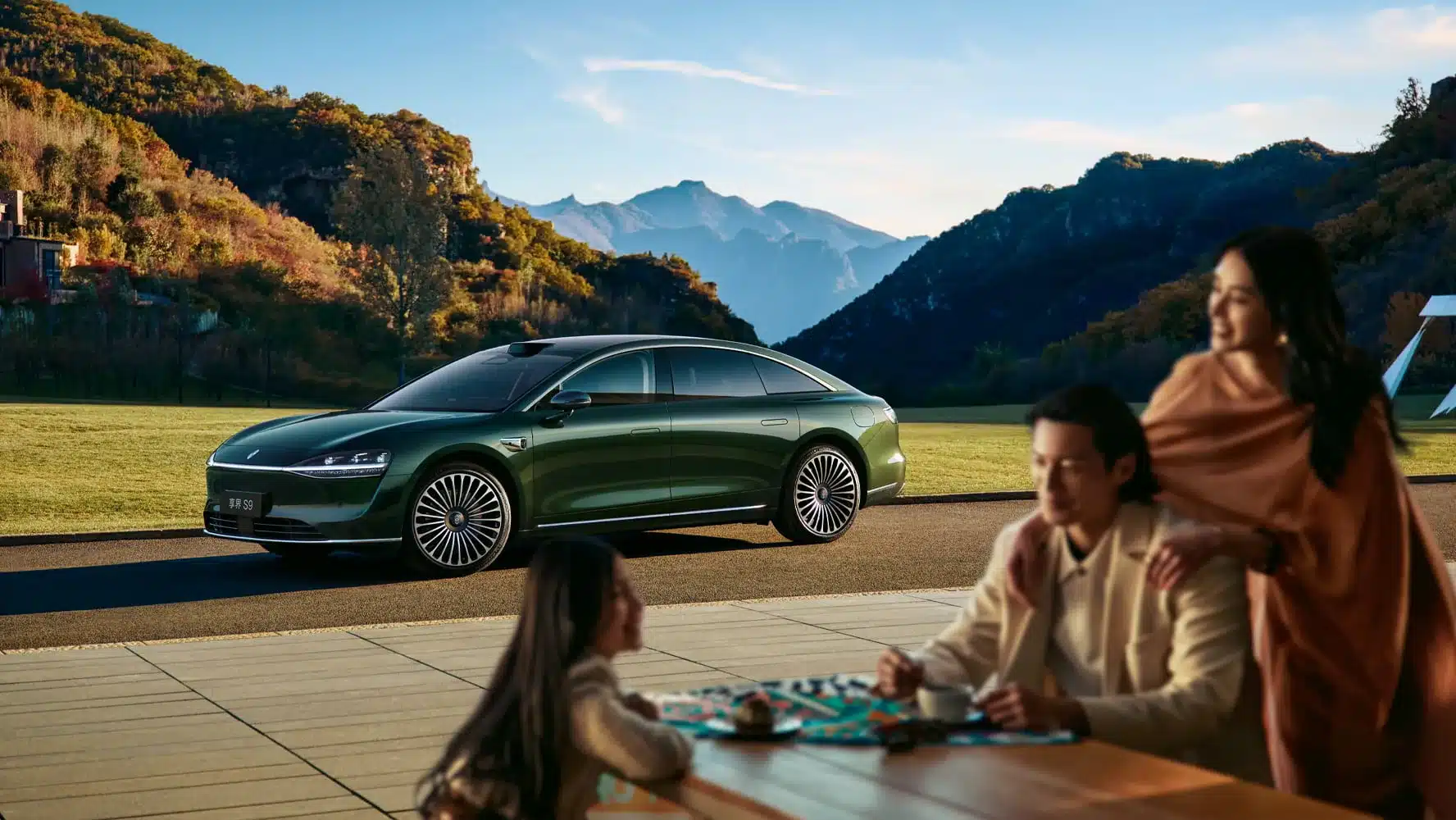 Grüne Xiangjie S9 Limousine geparkt vor malerischen Bergen, im Vordergrund eine Familie beim gemeinsamen Spiel.