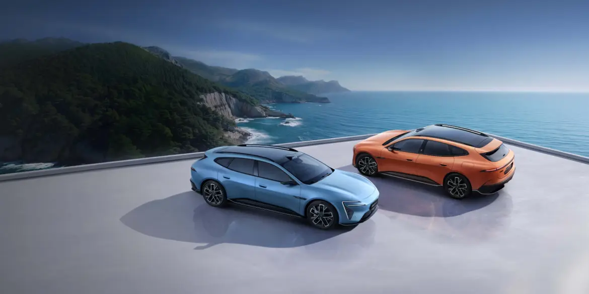 Zwei Avatr 06T Elektroautos, blau und orange, auf einer Plattform mit Blick aufs Meer und eine grüne Küstenlinie