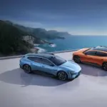 Zwei Avatr 06T Elektroautos, blau und orange, auf einer Plattform mit Blick aufs Meer und eine grüne Küstenlinie