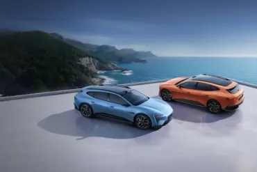 Zwei Avatr 06T Elektroautos, blau und orange, auf einer Plattform mit Blick aufs Meer und eine grüne Küstenlinie