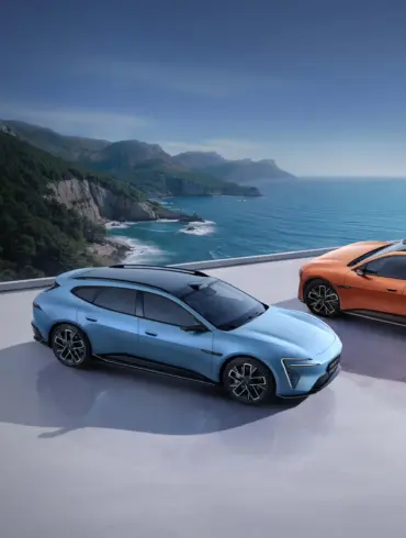 Zwei Avatr 06T Elektroautos, blau und orange, auf einer Plattform mit Blick aufs Meer und eine grüne Küstenlinie