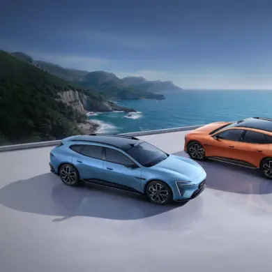 Zwei Avatr 06T Elektroautos, blau und orange, auf einer Plattform mit Blick aufs Meer und eine grüne Küstenlinie