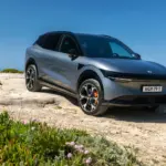 Silberner Zeekr 7X SUV geparkt auf einer Felsklippe mit Blick aufs Meer unter blauem Himmel.