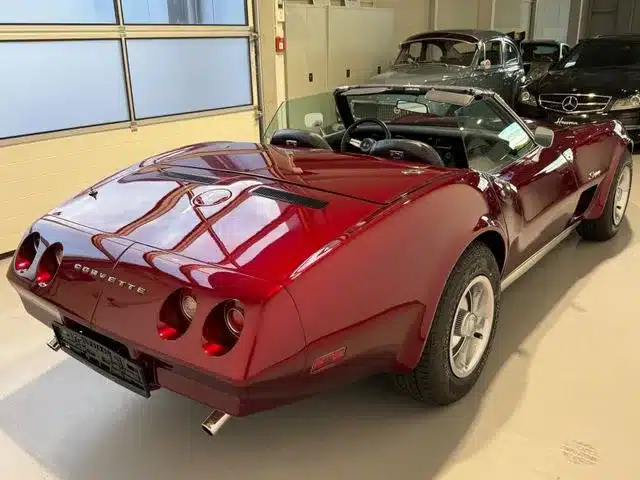 Chevrolet Corvette C3 Cabriolet in tiefrotem Candy-Lack von schräg hinten, mit geöffnetem Verdeck in einer Halle.