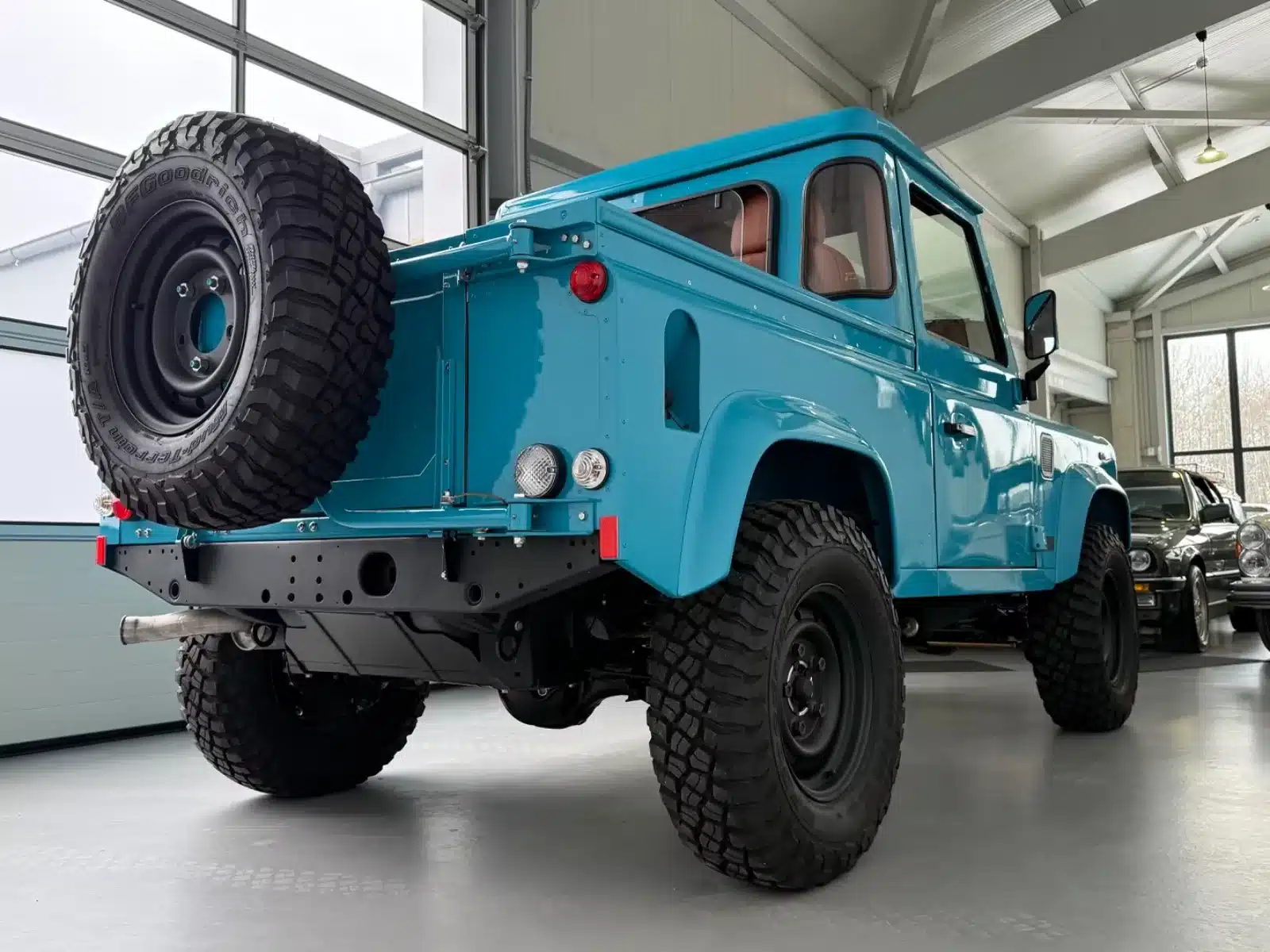 Blauer Land Rover Defender TD4 Alvarez One-of-One Showcar Monaco von hinten in einer modernen Garage, geländetaugliche Reifen, Ersatzrad heckseitig.