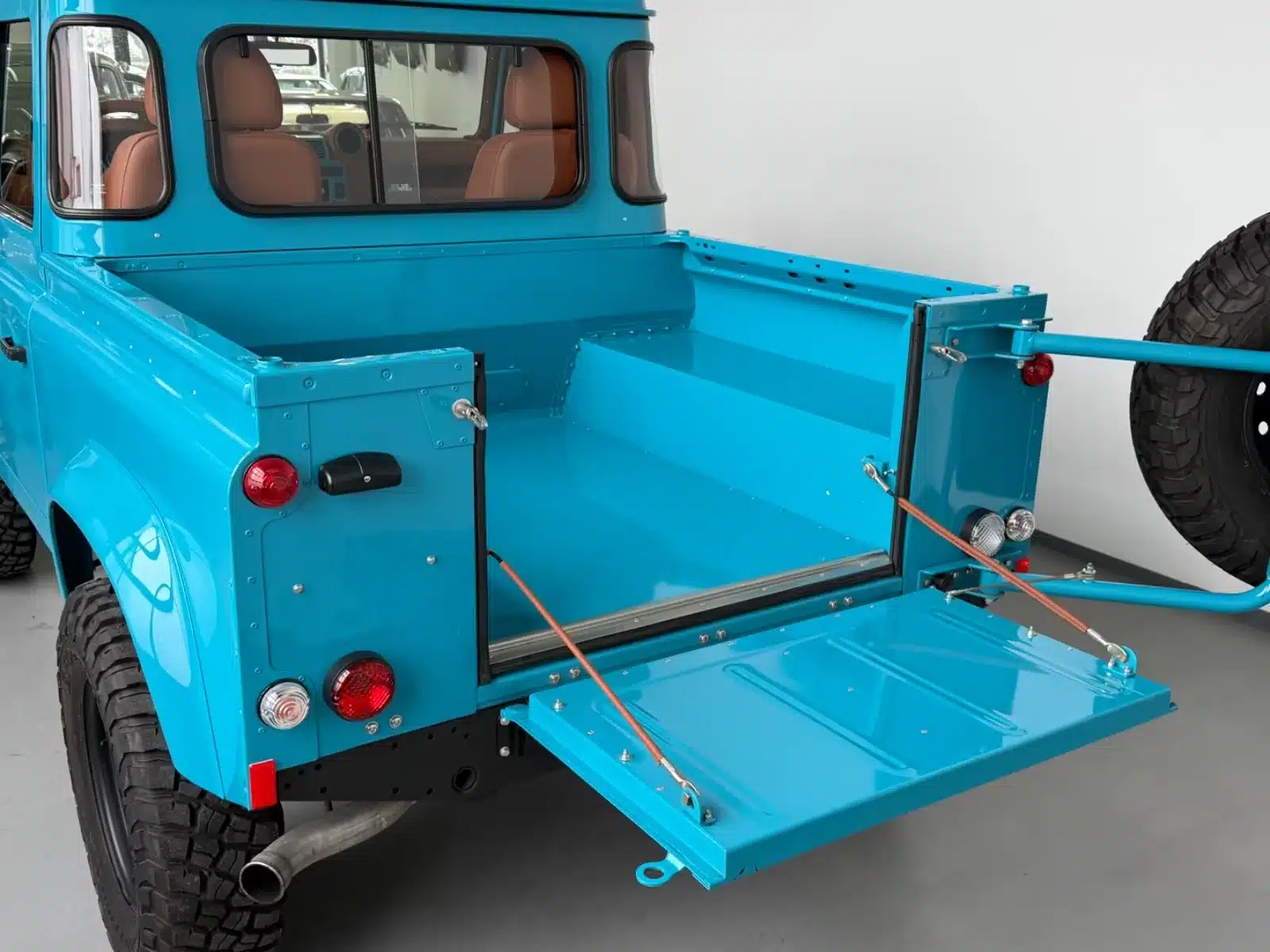 Rückansicht eines aufwendig restaurierten Land Rover Defender mit geöffneter Ladefläche in blauer Sonderlackierung.