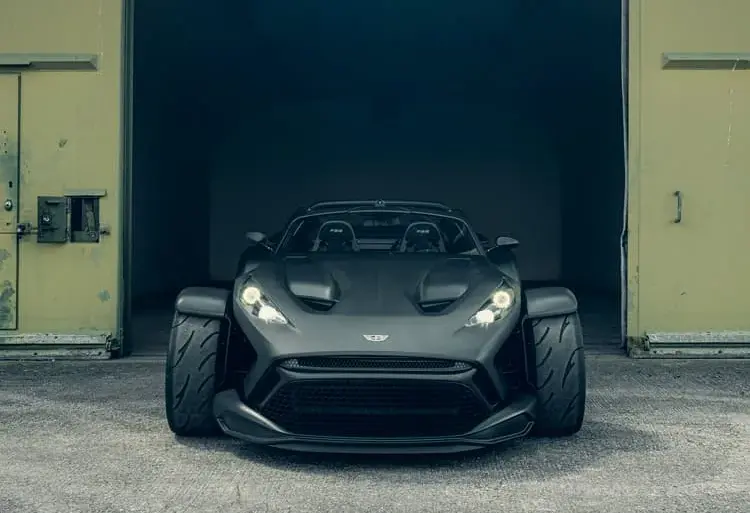 Frontansicht des Donkervoort F22 Bare Naked mit blanker Carbonfaser-Karosserie vor einer Industriehalle.