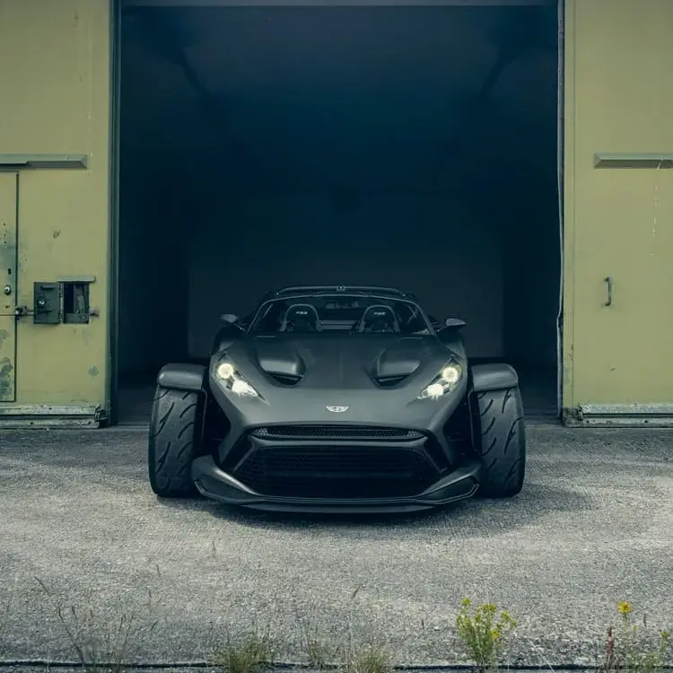 Frontansicht des Donkervoort F22 Bare Naked mit blanker Carbonfaser-Karosserie vor einer Industriehalle.