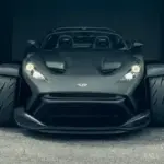 Frontansicht des Donkervoort F22 Bare Naked mit blanker Carbonfaser-Karosserie vor einer Industriehalle.