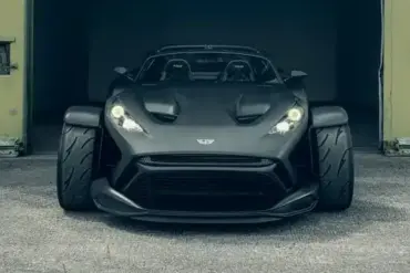 Frontansicht des Donkervoort F22 Bare Naked mit blanker Carbonfaser-Karosserie vor einer Industriehalle.