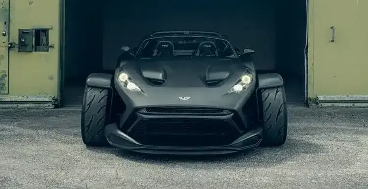 Frontansicht des Donkervoort F22 Bare Naked mit blanker Carbonfaser-Karosserie vor einer Industriehalle.
