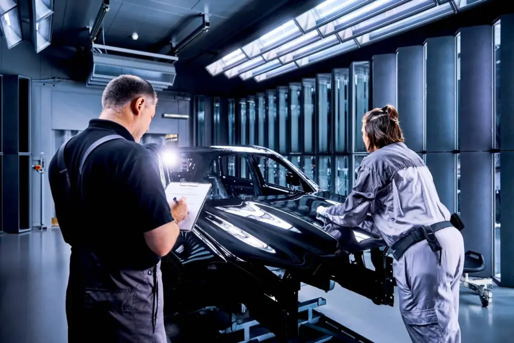 Zwei Mitarbeitende inspizieren die Karosserie eines schwarzen Elektroautos im Produktionswerk.