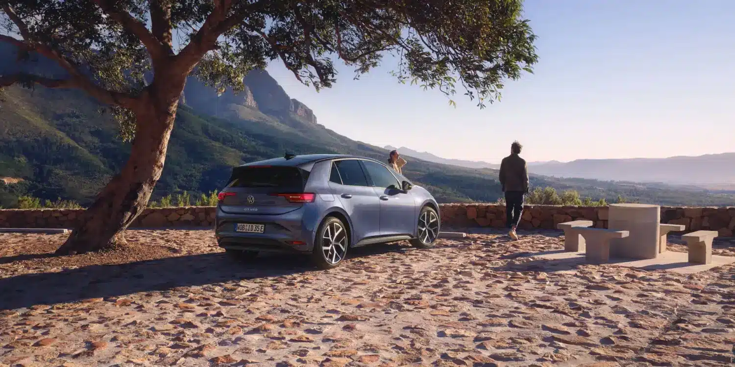 VW ID.3 Neo steht unter einem Baum mit Berglandschaft im Hintergrund