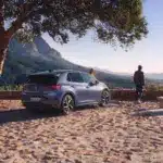 VW ID.3 Neo steht unter einem Baum mit Berglandschaft im Hintergrund