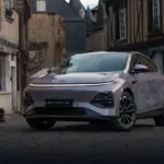 XPENG G6 Elektro-SUV in Metallic-Lackierung steht auf Kopfsteinpflaster vor alten Häusern.