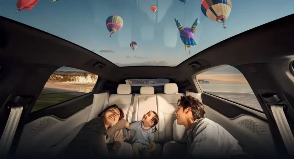 Innenraum des XPENG G6 mit Panoramadach, Familie entspannt auf der Rückbank, Ausblick auf Heißluftballons am Himmel.