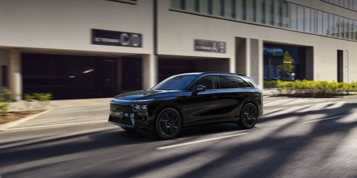 Schwarzer XPENG G9 SUV fährt auf einer sonnigen Straße vor Bürogebäuden.
