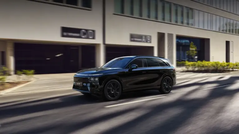 Schwarzer XPENG G9 SUV fährt auf einer sonnigen Straße vor Bürogebäuden.