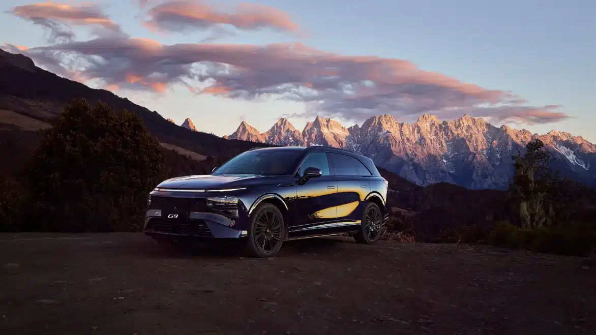 Schwarzer XPENG G9 Elektro-SUV steht vor Alpenbergen bei Sonnenuntergang auf einem Aussichtspunkt.