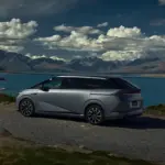 XPENG X9 fährt auf einer Uferstraße mit See und Bergen im Hintergrund.