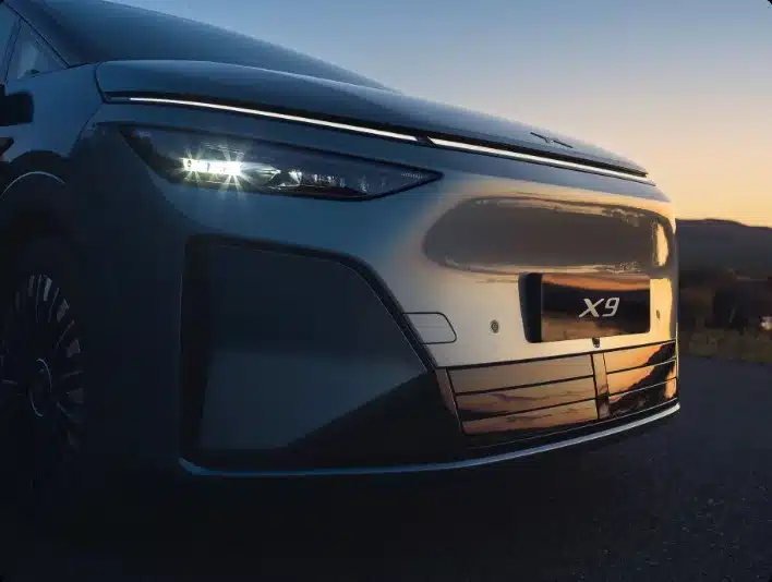 Frontansicht des XPENG X9 Elektro-Vans mit beleuchtetem Scheinwerfer und X9-Logo bei Sonnenuntergang