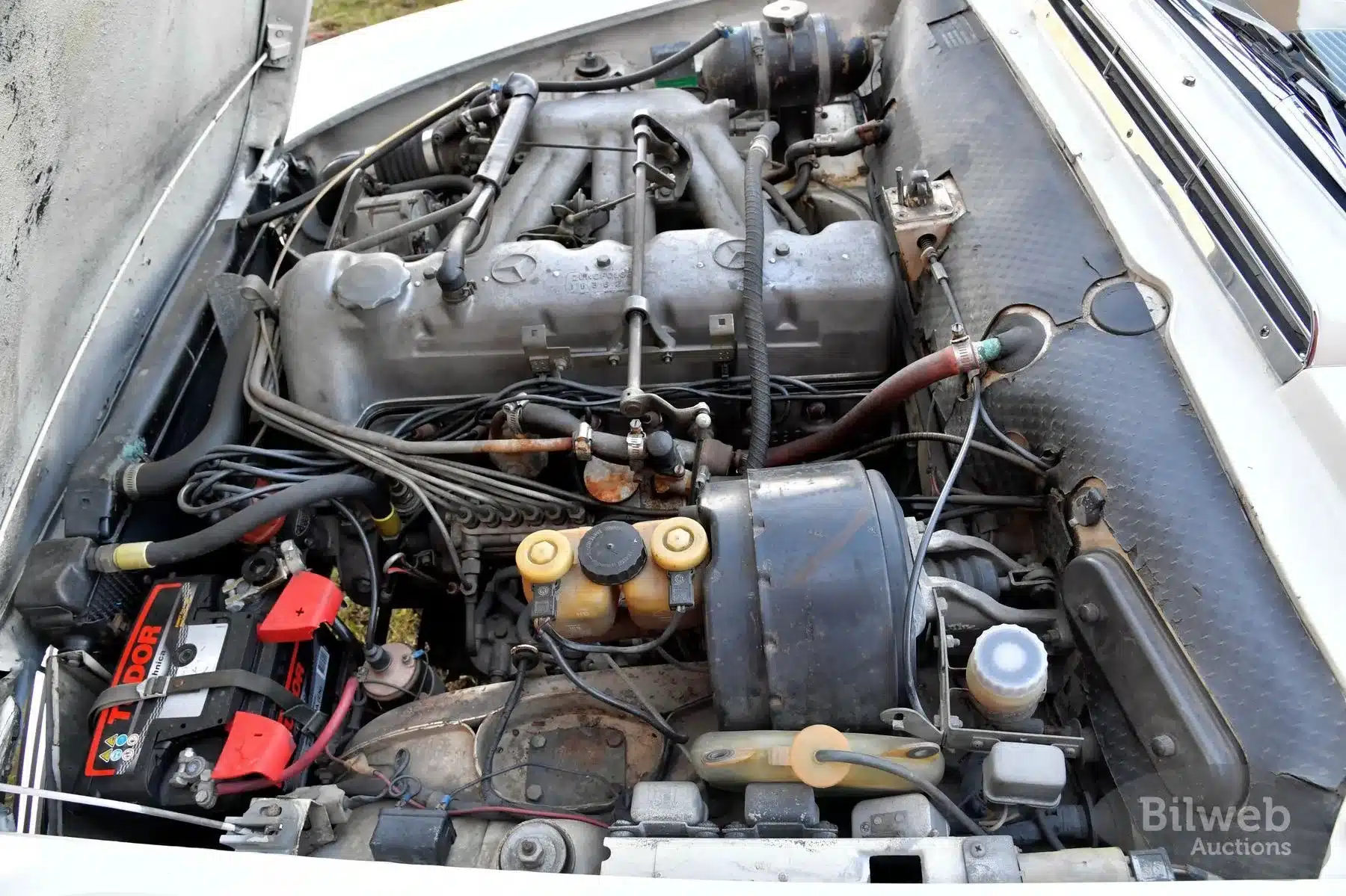Detailaufnahme des Motorraums eines Mercedes-Benz 280 SL Pagode W113, Baujahr 1968, mit sichtbarem Sechszylindermotor und altersbedingten Gebrauchsspuren