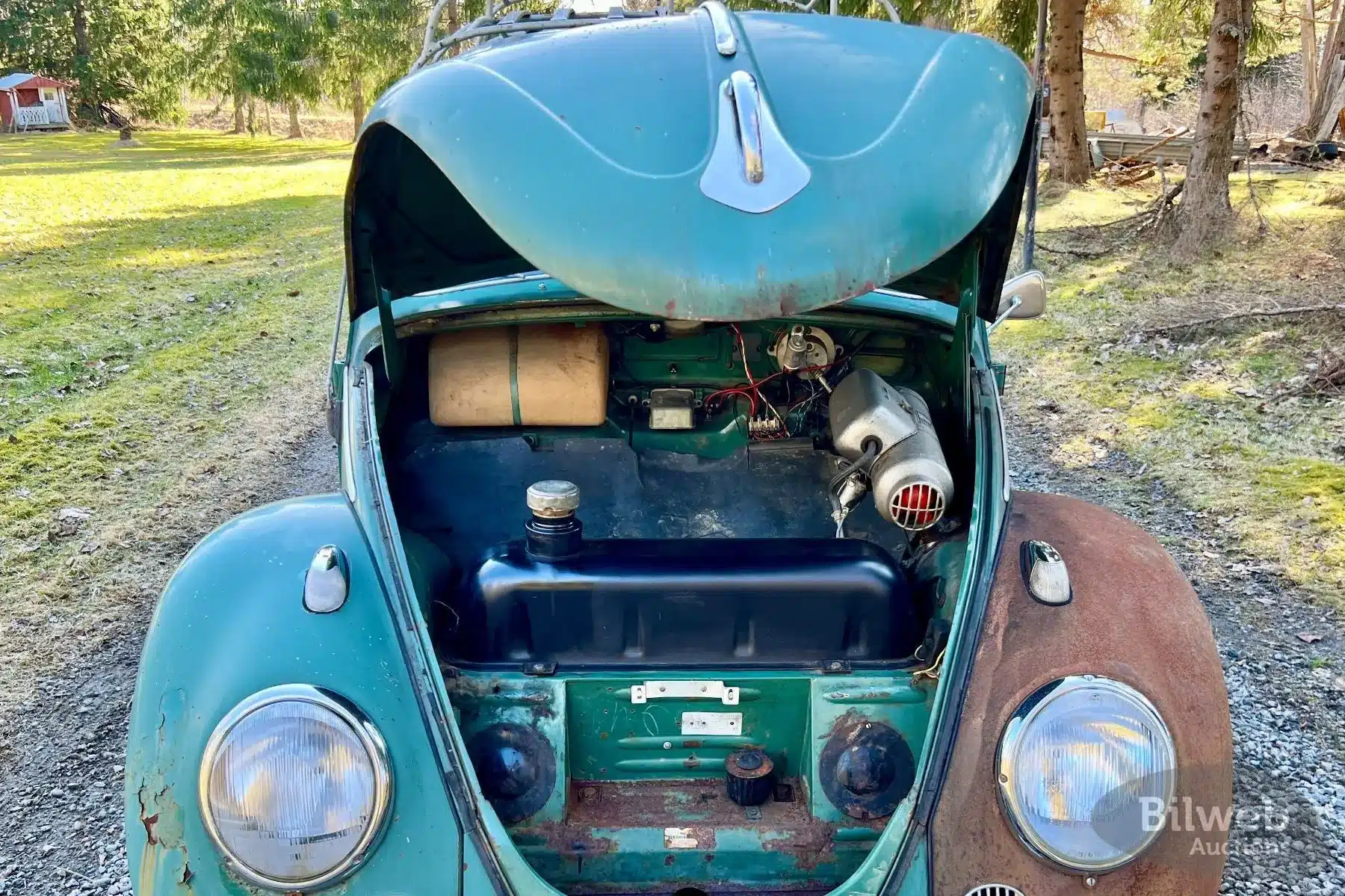 Frontansicht eines offenen Kofferraums eines unrestaurierten VW Käfer 1200 von 1960 mit sichtbarem Tank und Karosseriespuren.