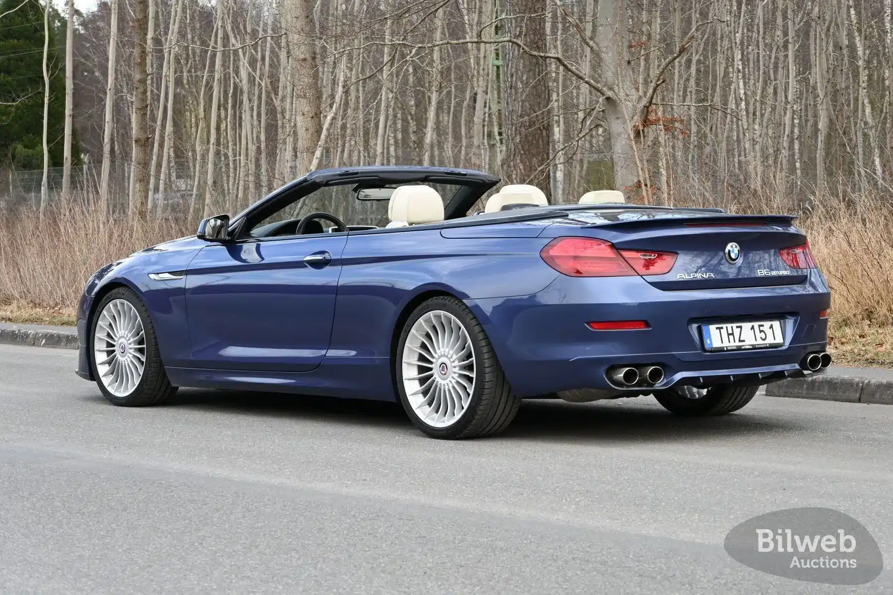 Heckansicht eines blauen Alpina B6 Biturbo Cabriolets von 2012 mit geöffnetem Verdeck auf einer Straße, umgeben von Bäumen.