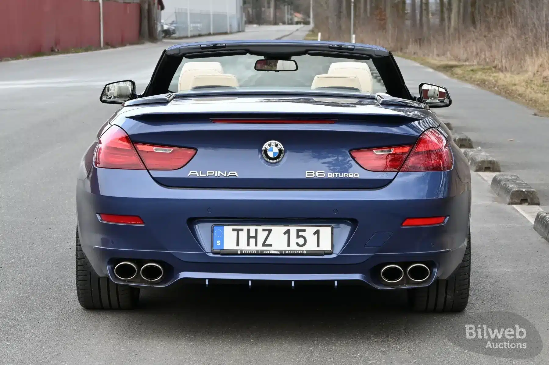 Heckansicht eines blauen Alpina B6 Biturbo Cabriolets mit geöffnetem Verdeck auf einer Straße.
