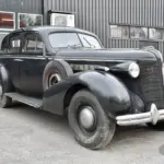 Schwarzer Buick Special Saloon Straight 8 von 1937 mit sichtbarer Patina und stilprägenden Details vor grauer Halle