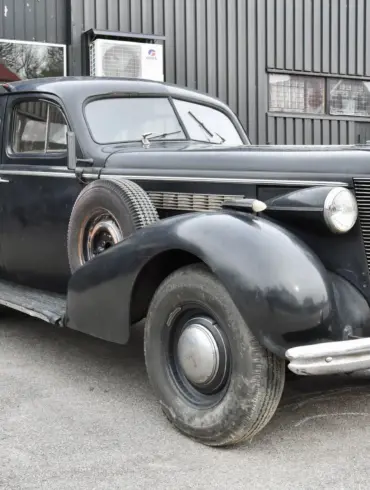 Schwarzer Buick Special Saloon Straight 8 von 1937 mit sichtbarer Patina und stilprägenden Details vor grauer Halle