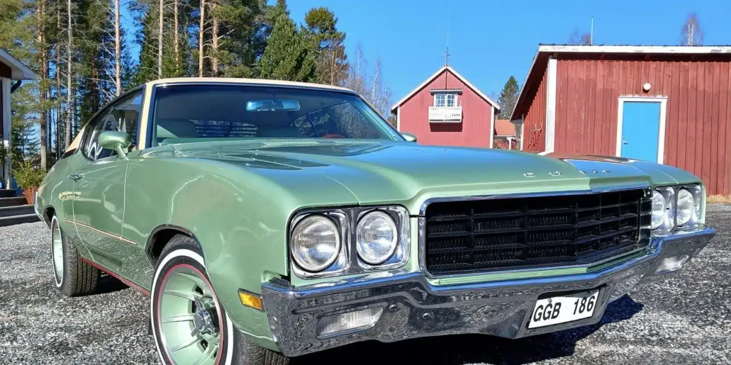 Grüner Buick Skylark Custom Sport Coupé V8 von 1970, fotografiert bei Tageslicht vor roten Häusern in Schweden.