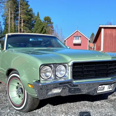 Grüner Buick Skylark Custom Sport Coupé V8 von 1970, fotografiert bei Tageslicht vor roten Häusern in Schweden.