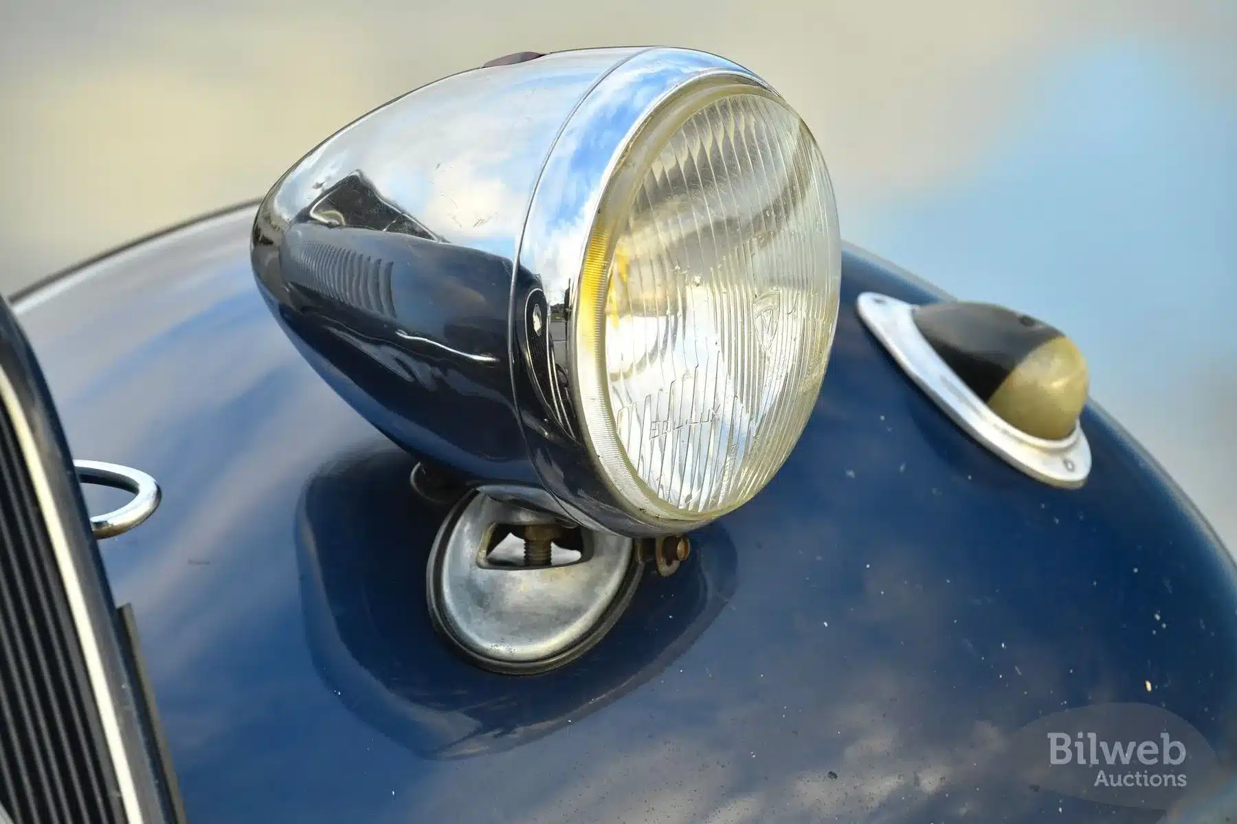 Nahaufnahme eines Chromscheinwerfers auf der Motorhaube eines Citroën B11 Traction Avant, Baujahr 1956, in dunkelblauer Lackierung mit Patina