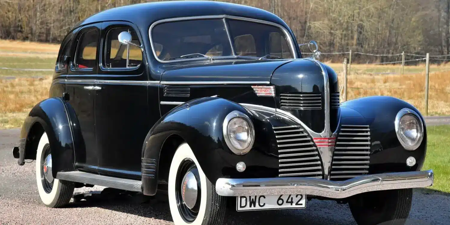 Schwarzer Dodge Senior Touring Sedan von 1939 mit weißwandbereifung, aufgenommen im Freien vor natürlicher Kulisse.
