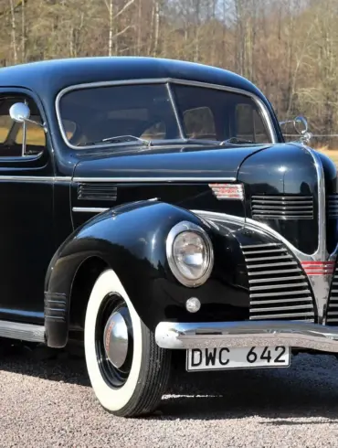Schwarzer Dodge Senior Touring Sedan von 1939 mit weißwandbereifung, aufgenommen im Freien vor natürlicher Kulisse.